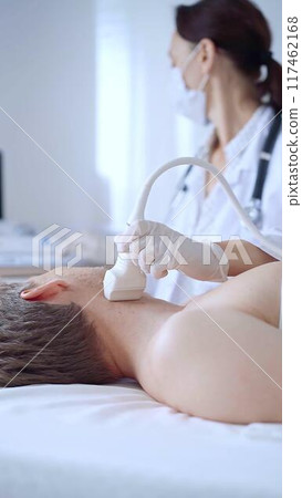 Doctor woman with white medical gloves performing neck ultrasound exam on male patient. Thyroid gland examination. Medicine concept Doctor woman with white medical gloves performing neck ultrasound exam on male patient. Thyroid gland examination. Medicine concept 117462168