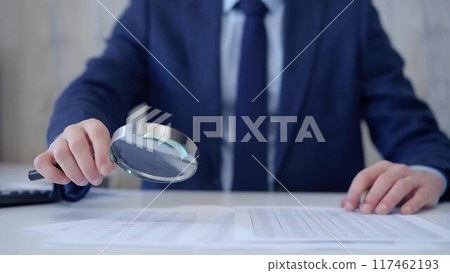 Businessman is carefully examining financial documents with a magnifying glass, highlighting the importance of thorough analysis in business. Audit and taxes Businessman is carefully examining financial documents with a magnifying glass, highlighting the importance of thorough analysis in business. Audit and taxes 117462193
