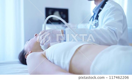 Doctor man with white medical gloves is using ultrasound machine to examine neck of female patient lying down in clinic. Medicine concept 117462206