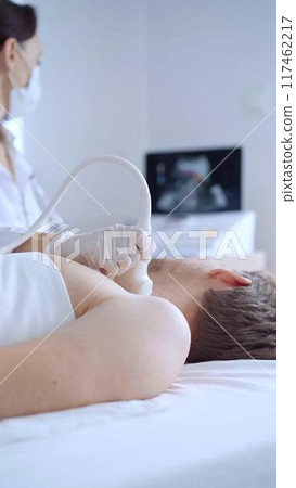 Doctor woman with white medical gloves performing neck ultrasound exam on male patient. Thyroid gland examination. Medicine concept 117462217