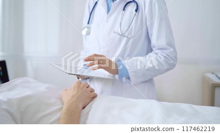 Doctor consulting patient with digital tablet in hospital room. Healthcare professional providing care 117462219