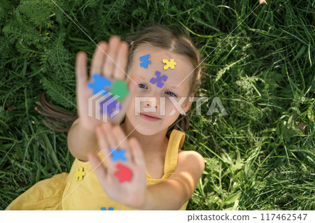 A girl strewn with multicolored paper puzzles. A symbol of awareness about autism A girl strewn with multicolored paper puzzles. A symbol of awareness about autism 117462547