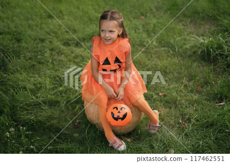 A cute adorable girl dressed up in a Halloween costume is sitting on big pumpkin. 117462551