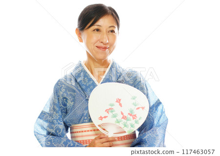 A smiling middle-aged woman wearing a high-quality silk yukata and holding a fan A smiling middle-aged woman wearing a high-quality silk yukata and holding a fan 117463057