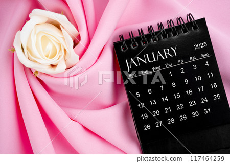 January 2025 desk calendar black color and rose on textile background. 117464259