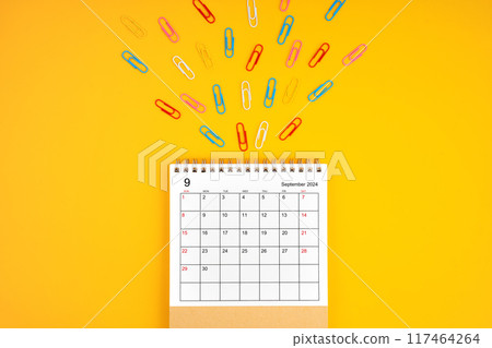 September 2024 desk calendar and colorful metal paperclips on yellow background. 117464264