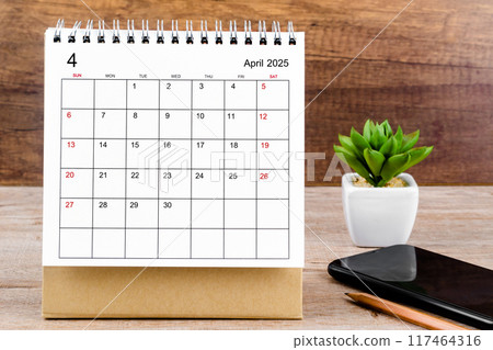 April 2025 desk calendar on wooden table with black smartphone. April 2025 desk calendar on wooden table with black smartphone. 117464316