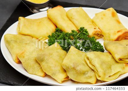 Golden baked crepes stuffed with savory filling, served with fresh parsley garnish on a white plate Golden baked crepes stuffed with savory filling, served with fresh parsley garnish on a white plate 117464333