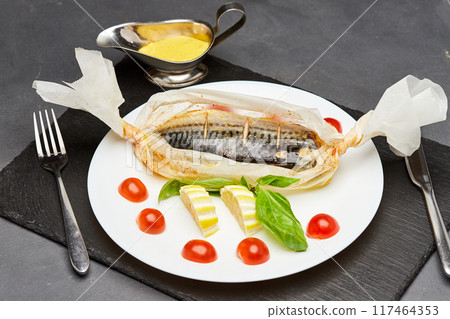 Gourmet baked mackerel in parchment with lemon slices, basil, and cherry tomatoes 117464353