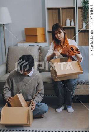 Young Asian couple relocating to a new house, joyfully packing and unpacking belongings. Expertise in moving, packing, togetherness, and creating a new home together. 117464601