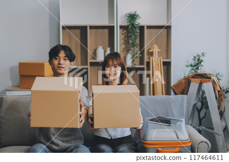 Young Asian couple relocating to a new house, joyfully packing and unpacking belongings. Expertise in moving, packing, togetherness, and creating a new home together. Young Asian couple relocating to a new house, joyfully packing and unpacking belongings. Expertise in moving, packing, togetherness, and creating a new home together. 117464611