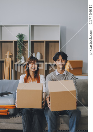 Young Asian couple relocating to a new house, joyfully packing and unpacking belongings. Expertise in moving, packing, togetherness, and creating a new home together. 117464612