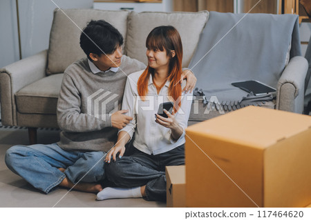 Young Asian couple relocating to a new house, joyfully packing and unpacking belongings. Expertise in moving, packing, togetherness, and creating a new home together. Young Asian couple relocating to a new house, joyfully packing and unpacking belongings. Expertise in moving, packing, togetherness, and creating a new home together. 117464620