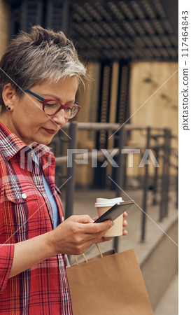 A woman is actively engaged in mobile shopping while enjoying the outdoors in the city 117464843