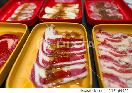 Slices of raw meat arranged on yellow and red trays, ready to be cooked, most likely for barbecue or grilling. 117464953