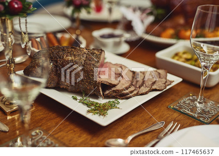 Holiday lunch, home or table with roast beef for Christmas meal, cut meat or luxury cooking in house. Vacation, kitchen or grill steak for protein with festive season, party with food for wellness Holiday lunch, home or table with roast beef for Christmas meal, cut meat or luxury cooking in house. Vacation, kitchen or grill steak for protein with festive season, party with food for wellness 117465637