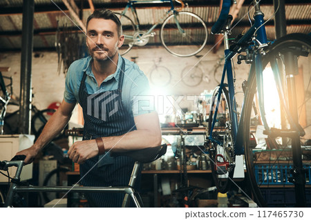 Man, bicycle shop and portrait for maintenance job, startup with transport service. Bike, mechanic and male entrepreneur in workshop with serious face, professional or sustainable business with apron 117465730