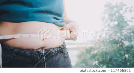 fat woman, fat belly, chubby, obese woman hand holding excessive belly fat with measure tape, woman diet lifestyle concept 117466861