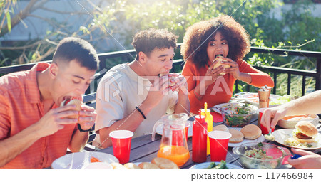 Friends, group and eating hamburger outdoor on terrace with hunger, reunion and social event in summer. People, barbecue and lunch on patio with food, diversity or celebration with bonding and drinks 117466984