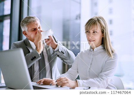 Blowing nose, tissue and businessman with coworker, desk and allergies or hayfever in office Sick or flu and computer for typing for mature male person, virus or influenza for infection with sneeze 117467064
