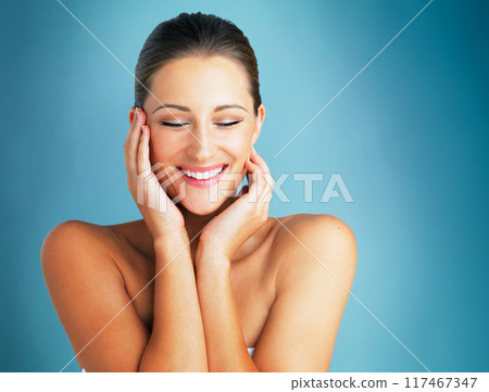 Woman, beauty and happy from skincare, wellness and facial treatment in a studio. Makeup, cosmetics and dermatology with relax and calm skin care with blue background and smile from glow and shine 117467347