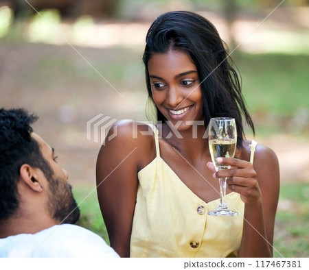 Couple, champagne and smile in nature for summer vacation, relax and happiness for relationship. Indian, happy and celebration, man and woman in park with drinks for love, romance or anniversary date 117467381