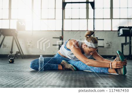 Fitness, legs and stretching with woman on floor of gym for health, routine or wellness. Exercise, training or warm up for workout and athlete getting ready for physical improvement with music 117467450