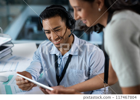 The customer care department is getting bigger by the day. Shot of a young man and woman using a digital tablet while working in a call centre. The customer care department is getting bigger by the day. Shot of a young man and woman using a digital tablet while working in a call centre. 117467804