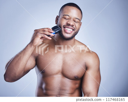 Man, electric shaver and beard in studio for skincare, grooming or facial hair removal with epilation. Topless, black person or happy with shaving for personal hygiene or self care on blue background Man, electric shaver and beard in studio for skincare, grooming or facial hair removal with epilation. Topless, black person or happy with shaving for personal hygiene or self care on blue background 117468165