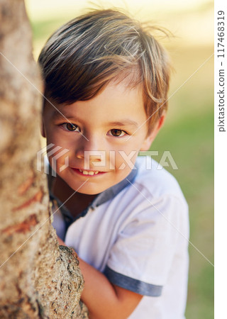 Boy, hide and happy by tree for portrait in park for games, adventure and outdoor for playing in summer. Child, nature and shy smile in forest for holiday, vacation and freedom for growth in Canada 117468319