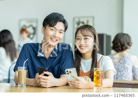 A young couple looking at a smartphone at a cafe 117468365