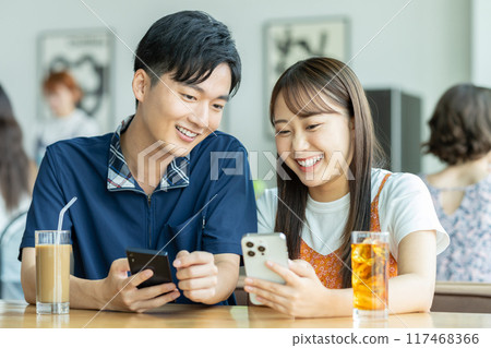 A young couple looking at a smartphone at a cafe A young couple looking at a smartphone at a cafe 117468366