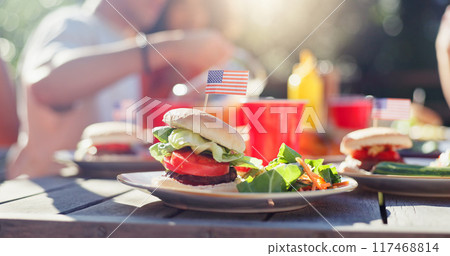 Hamburger, food and salad on plate outdoor at reunion lunch for national independence day. American flag, vegetables and patty on bun by wooden table for United states holiday event in backyard. 117468814
