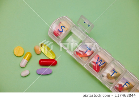 Wellness, daily medicine and pill box in studio for prescription, healthcare or capsule on green background. Above, health and plastic container with drugs for vitamin D, supplements or mockup 117468844