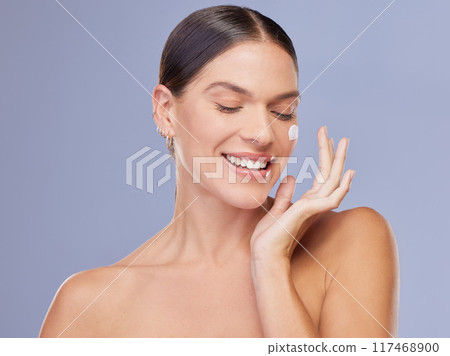 Happy woman, face cream and beauty product application in studio for wellness, dermatology or collagen on purple background. Smile, sunscreen and girl model with spf, lotion or facial acne treatment 117468900