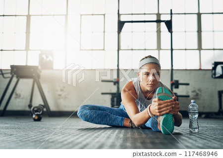 Fitness, legs and stretching with woman on floor of gym for health, wellness or workout. Exercise, music and warm up for training with serious athlete getting ready for physical improvement routine 117468946