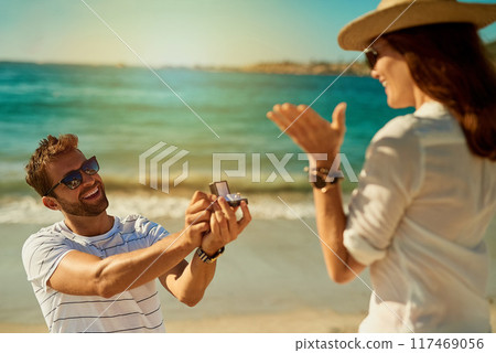 Love, engagement and couple on a beach, happy and relationship for commitment, vacation and support. Surprise, man and woman on seaside holiday, proposal and ask for hand in marriage for romance 117469056