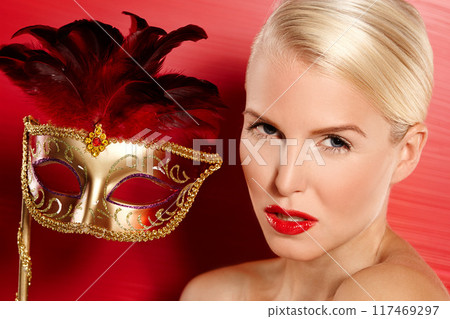 Portrait, confidence and woman in carnival mask for beauty, art deco and dress up by red background. Cosmetics, female person and mysterious or playful with fantasy, lipstick and cosplay in studio 117469297