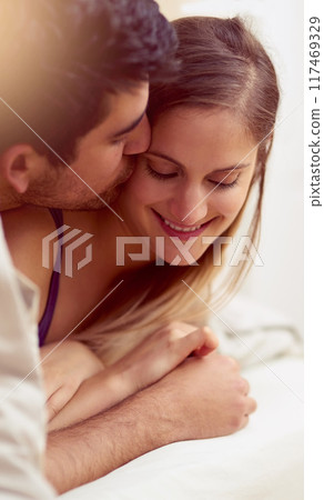 Couple, love and affection in bed with kiss with intimacy for dating or marriage in house with smile. Romance, honeymoon and embrace with touching for bonding with care in relationship with duvet. 117469329