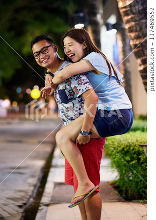 Couple, piggyback and city or laughing for travel adventure or romance, funny or happiness. Asian man, woman and downtown date in Bali for sightseeing night on summer vacation for joke, humor or trip 117469552