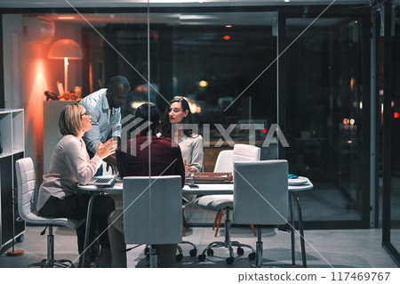 Business people, laptop and teamwork for design at night in office, creative agency and project overtime. Planning, support and problem solving in research meeting for deadline and discussion 117469767