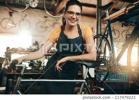 Woman, bicycle shop and portrait for maintenance job, startup with transport service. Bike, mechanic and female entrepreneur in workshop with glasses, happiness for sustainable business with apron 117470221