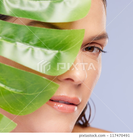 Woman, half face and leaf for cosmetics in studio, skincare and vegan or organic beauty on blue background. Female person, skin detox and eco friendly or facial treatment, dermatology and plant 117470491