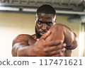 Black bodybuilder concentrating on stretching his wrists 117471621