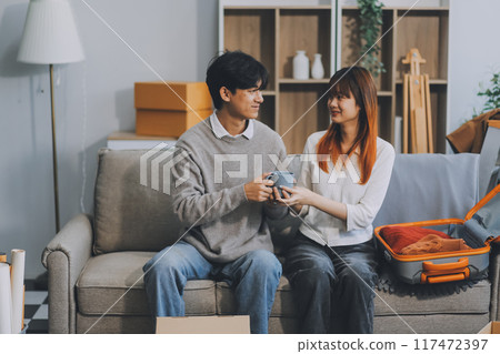 Young Asian couple relocating to a new house, joyfully packing and unpacking belongings. Expertise in moving, packing, togetherness, and creating a new home together. Young Asian couple relocating to a new house, joyfully packing and unpacking belongings. Expertise in moving, packing, togetherness, and creating a new home together. 117472397