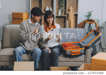 Young Asian couple relocating to a new house, joyfully packing and unpacking belongings. Expertise in moving, packing, togetherness, and creating a new home together. 117472400