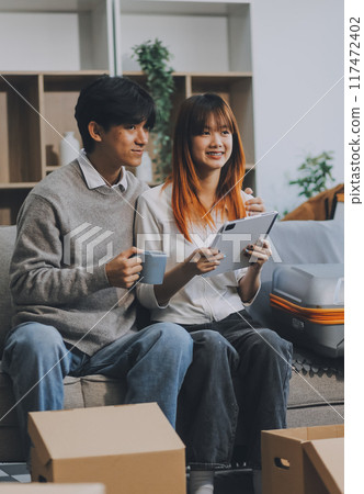 Young Asian couple relocating to a new house, joyfully packing and unpacking belongings. Expertise in moving, packing, togetherness, and creating a new home together. Young Asian couple relocating to a new house, joyfully packing and unpacking belongings. Expertise in moving, packing, togetherness, and creating a new home together. 117472402