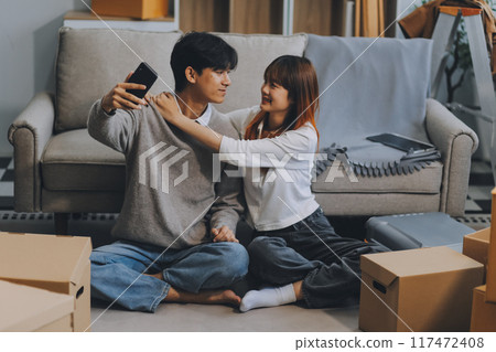 Young Asian couple relocating to a new house, joyfully packing and unpacking belongings. Expertise in moving, packing, togetherness, and creating a new home together. Young Asian couple relocating to a new house, joyfully packing and unpacking belongings. Expertise in moving, packing, togetherness, and creating a new home together. 117472408