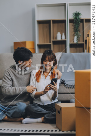 Young Asian couple relocating to a new house, joyfully packing and unpacking belongings. Expertise in moving, packing, togetherness, and creating a new home together. 117472412