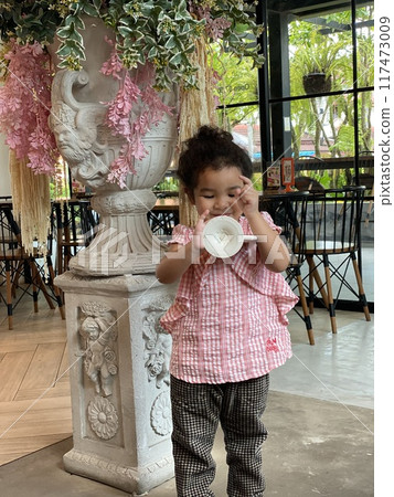 Cute little girl drinking milk from a plastic cup in a cafe 117473009